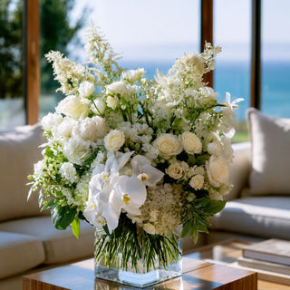 Styled artificial white true bloom real touch floral arrangement in a vase on a marble coffee table in a luxury modern home with coastal views