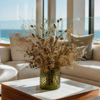 Luxury faux acorn botanical arrangement featuring brown acorn stems, preserved olive branches, smoke bush, eucalyptus, and dried grasses styled in an olive green glass vase for elegant autumn home décor.
