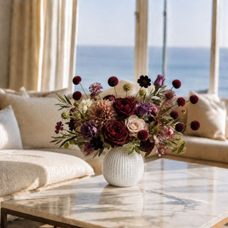 "Luxury burgundy faux floral arrangement featuring burgundy pom pom stems, wine garden roses, taupe dahlias, antique mauve roses, chocolate cosmos and olive foliage styled in a textured white ceramic vase for elegant fall home decor