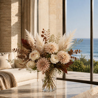 True Bloom Floral luxury faux floral arrangement featuring blush dahlias, ivory roses, flocked cream pampas grass, burgundy magnolia foliage and warm autumn greenery in a clear glass cylinder vase. Styled in a California coastal home with ocean views, this elegant modern fall centerpiece brings timeless, high-end botanical design to luxury interiors.