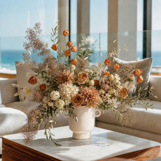 Luxury faux dried Chinese lantern floral arrangement featuring burnt orange Physalis stems, Café au Lait dahlias, ivory hydrangeas, toffee roses, preserved smoke bush, olive branches, bunny tails, and dried grasses styled in a modern ivory ceramic vase. This elegant autumn centerpiece is ideal for fall home décor, luxury interior styling, seasonal table décor, and high-end faux floral arrangements.