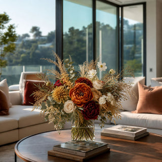 Luxury faux autumn floral arrangement featuring burnt orange peonies, Café au Lait dahlias, ivory roses, sunflowers, olive branches, and preserved botanicals styled in a clear glass vase for elegant fall home décor.