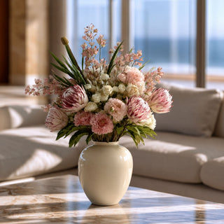 Purple flocked king protea faux floral arrangement styled in a cream ceramic vase with blush and neutral florals in a modern luxury living room setting.