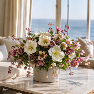 True Bloom Floral faux hellebore arrangement with realistic white and blush blooms, airy pink accents, and lush greenery in a modern ceramic vase. Styled on a marble coffee table in a luxury coastal-inspired living room, showcasing premium artificial flowers designed for elegant home décor.
