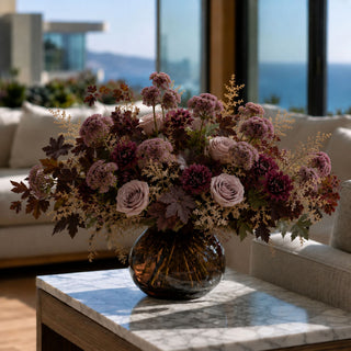 Luxury fall floral arrangement with dusty mauve sedum, burgundy dahlias, blush roses and autumn foliage in a smoky amber glass vase, styled by True Bloom Floral in an elegant California coastal home