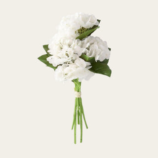 White real touch hydrangea 6-stem bundle with soft rounded blooms, faux green leaves, and flexible stems tied together, ideal for year-round floral arrangements because the crisp white color pairs easily with seasonal greenery, warm neutrals, and refined holiday accents.
