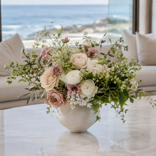 White Berry and Herb Bundle of 3 Stems styled as soft filler and texture in a floral arrangement with cream roses, white ranunculus-style blooms, pale pink accent flowers, seeded greenery, and layered foliage in a neutral vase on a marble coffee table in a bright coastal living room.