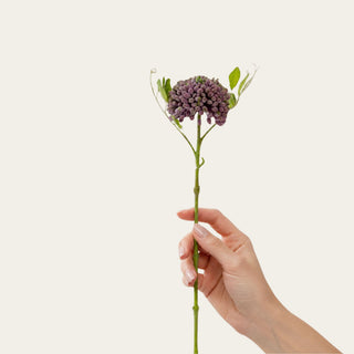 Woman's hand holding a Purple Real Touch Sedum Stem featuring realistic clustered buds with a natural chalk-like finish and flexible stem, ideal for adding texture, movement, and layered dimension to arrangements with hydrangeas, peonies, roses, and seasonal greenery throughout spring, summer, fall, and winter decorating.