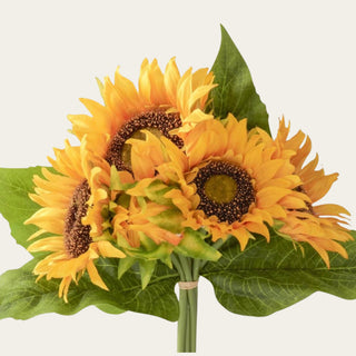 Close-up of yellow artificial sunflower blooms with layered fabric and polyester petals, textured brown centers and broad green leaves.
