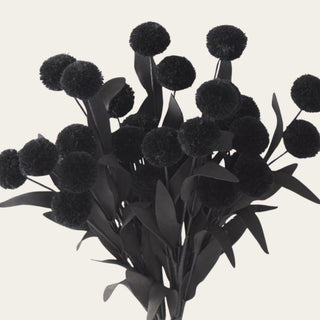 Close-up of black fuzzy pom-pom flowers with matte EVA leaves, showing the soft textured surface and dark faux foliage detail used for contrast in arrangements.