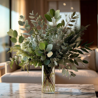 Luxury faux eucalyptus and mixed greenery arrangement in a clear glass vase on a marble coffee table, styled in a bright modern coastal living room with ocean view and soft natural sunlight, elegant high-end home decor