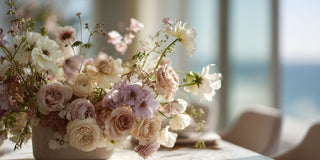 a refined floral arrangement composed of floral stems in soft blush pink, creams, and soft sage green tones, light lavender and with gentle variation in petal layering