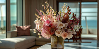 Floral arrangement in a vase on a table with a blurred background of a living room and ocean view.