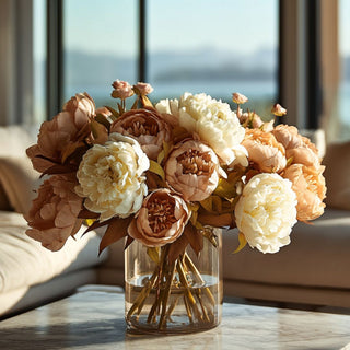 Taupe and neutral peony faux floral arrangement in a glass vase on a marble coffee table, styled in a modern coastal living room with warm natural light and ocean view