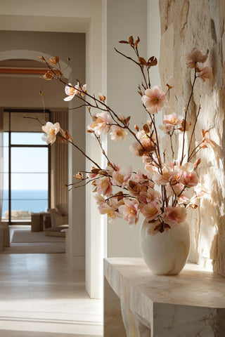 Luxury faux blush floral branch arrangement in a sculptural vase styled on an entryway console table in a bright modern coastal home with natural sunlight, elegant high-end interior styling