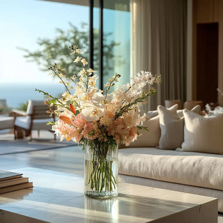 Luxury faux orchid and peach floral arrangement in a clear glass vase on a marble coffee table, styled in a bright coastal living room with ocean view and soft natural sunlight, elegant high-end home decor